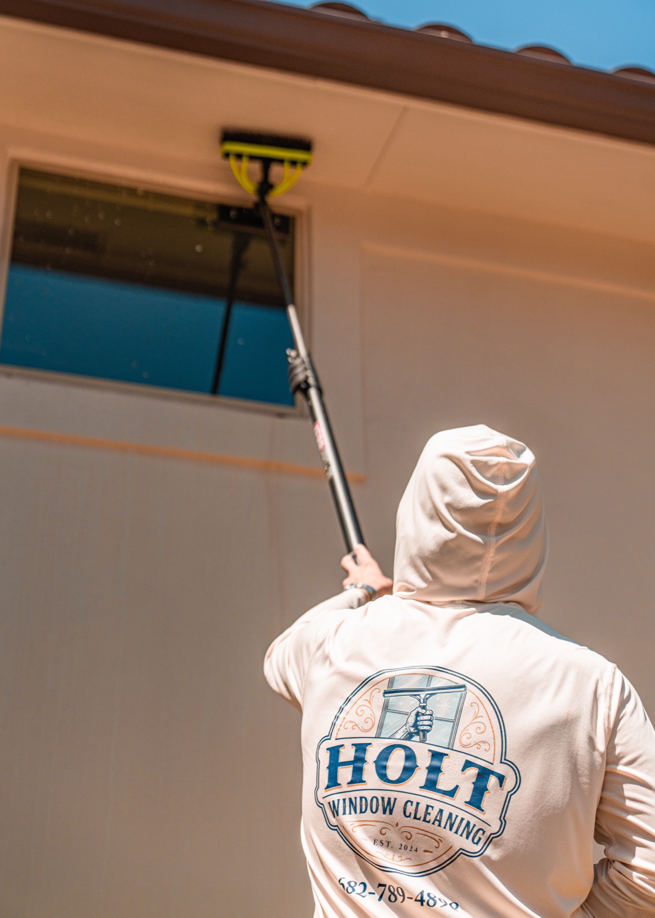 Caleb in a Holt Window Cleaning shirt raising a pole to an upper window.