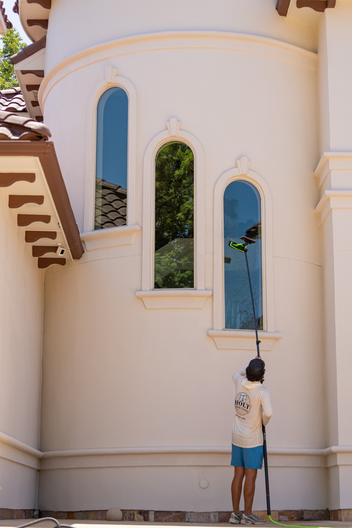 Caleb reaching the arched turret windows of a stucco home with a water-fed pole.