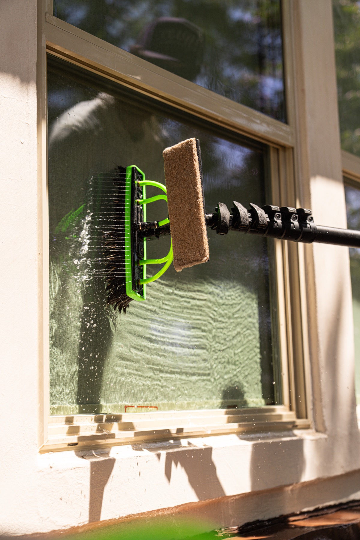 Close view of a brush and squeegee head drawing down a soapy pane of glass.