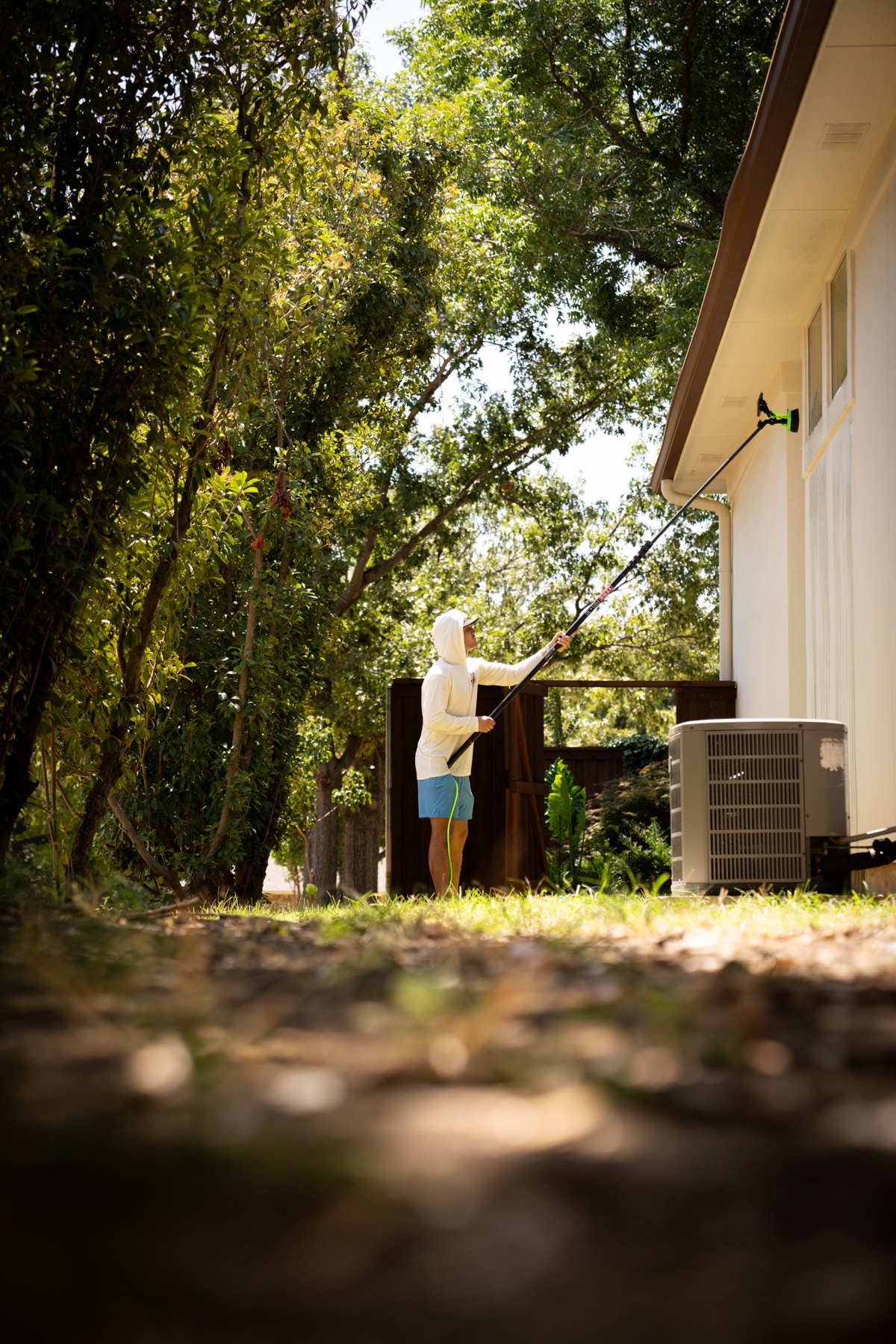 Caleb working along the shaded side of a house, in among the trees.